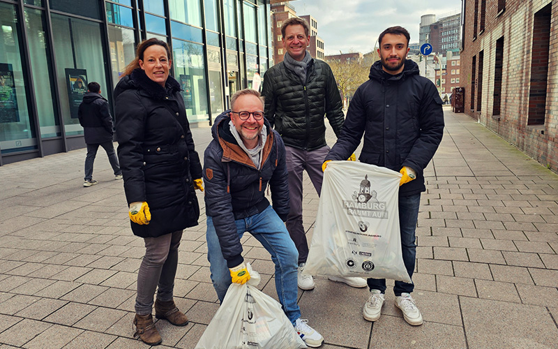 Vier Mitarbeiter der GEV stehen mit Müllbeuteln in der Hand in einer Fußgängerzone in der Hamburger Innenstadt. Sie nehmen teil an der Aktion 'Hamburg räumt auf'