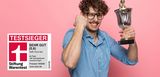 Zum 3. Mal Testsieger für überragend guten Wohngebäudeversicherungs-Tarif. Wir sind stolz darauf!  Junger Mann mit Bart und Brille hält jubelnd einen Siegerpokal in der Hand.