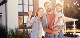 Einziehen, aufatmen, absichern – weil zum Traumhaus auch ein gutes Sicherheitsnetz gehört Junges Paar mit Kind steht glücklich vor dem neuen Eigenheim und hält den Hausschlüssel in der Hand – Symbol für sicheren Hauskauf und passenden Versicherungsschutz